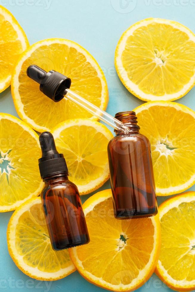 frasco de vidro marrom com um soro de pipeta com vitamina c. óleo essencial e fatias de laranja. conceito de saúde e beleza. foto