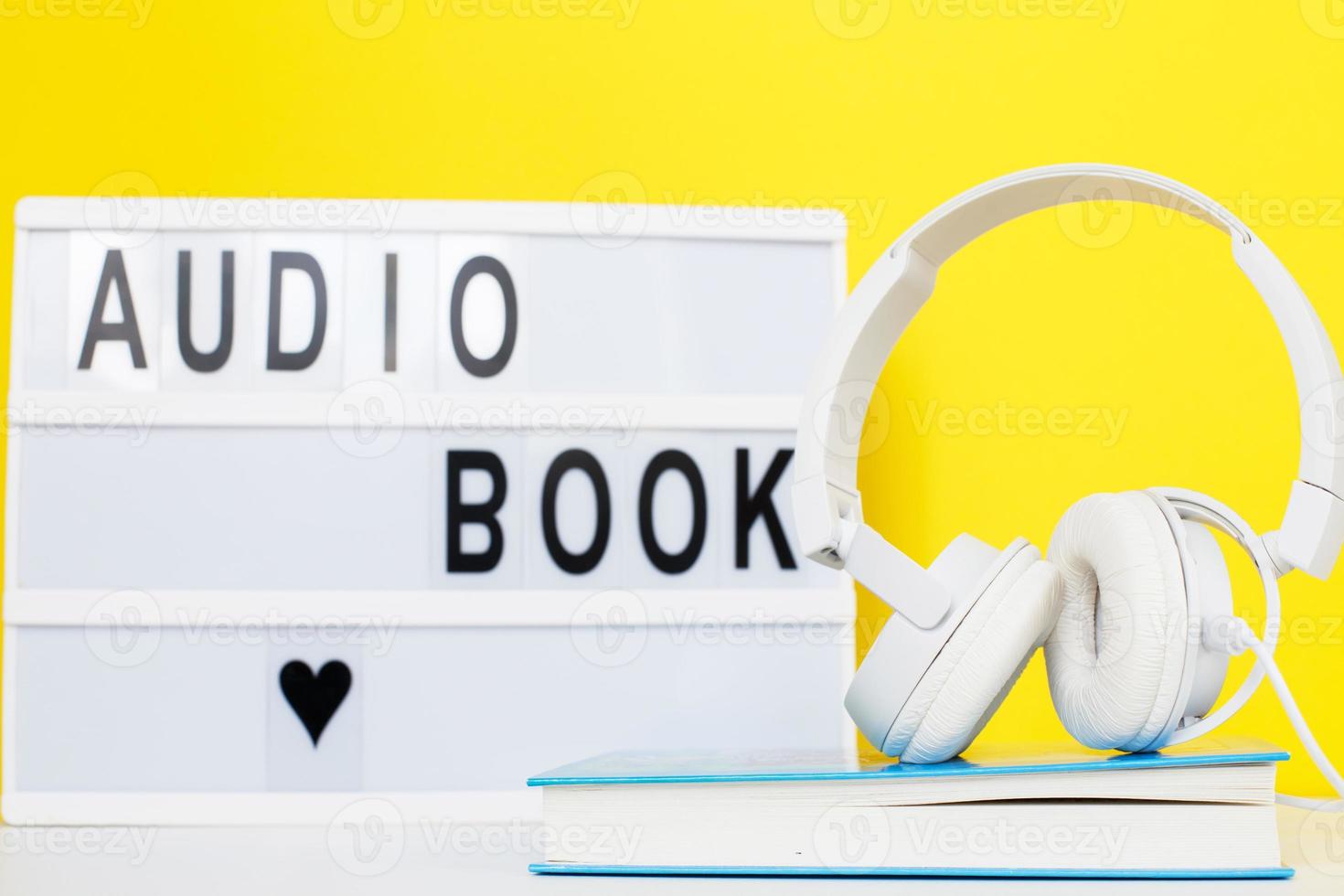 conceito de livro de áudio com fones de ouvido brancos modernos e livro de capa dura em um fundo amarelo. inscrição em uma mesa de luz foto