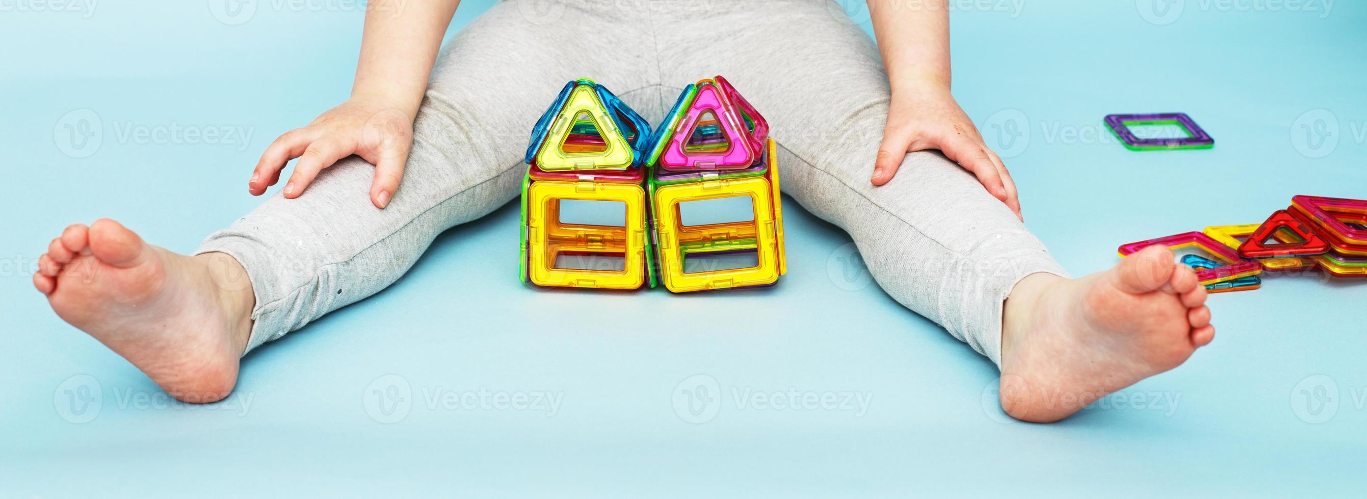 menina brincando com brinquedo construtor magnético colorido sobre fundo azul. criança construiu uma casa. bandeira foto