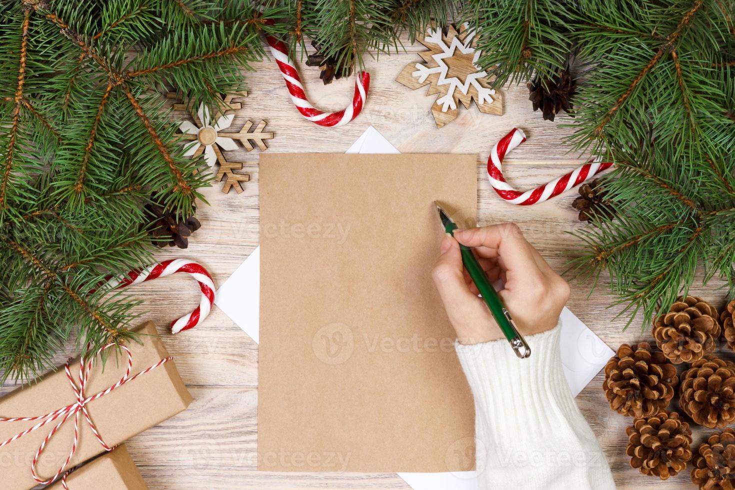 mãos femininas escrevendo uma carta para o papai noel. presentes de natal em um fundo de madeira. vista de cima foto