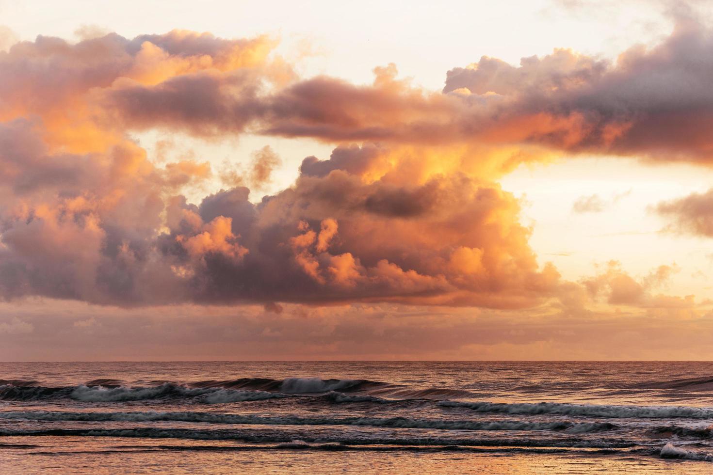 nuvens fofas do pôr do sol acima das ondas foto