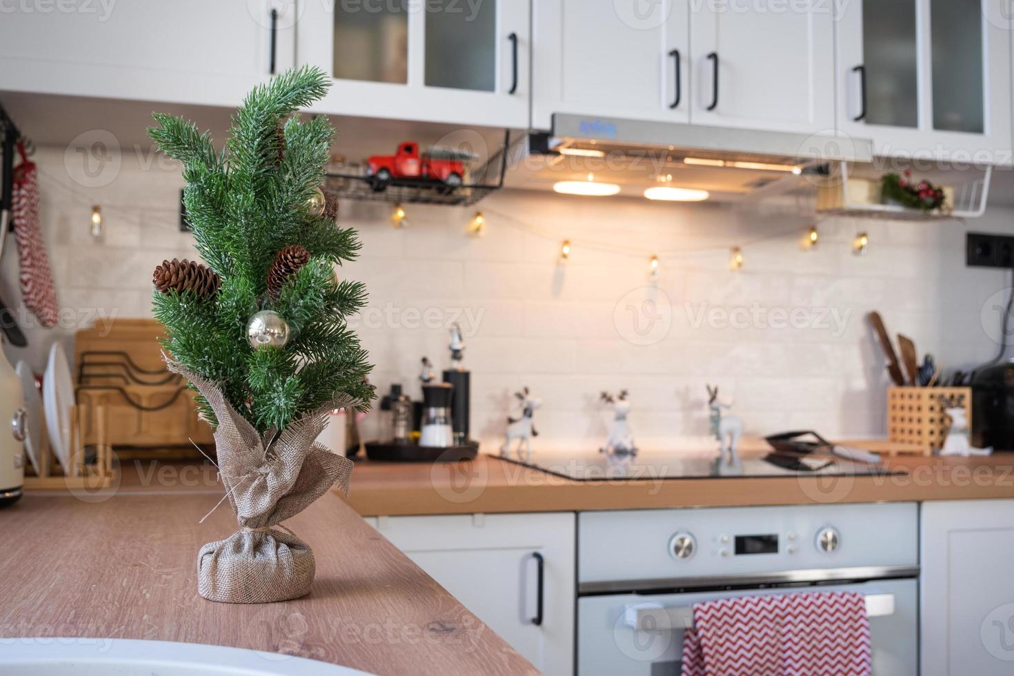 decoração de cozinha de natal - preparação para férias em família, luz de fadas, árvore de natal, enfeite vermelho, veado engraçado em armários, fogão. clima de celebração, véspera, ano novo foto