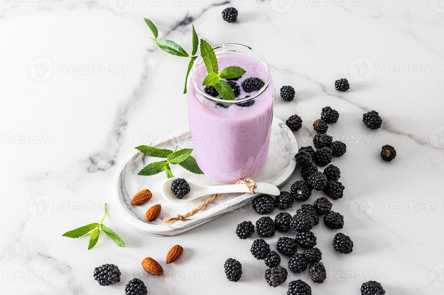 um copo de vidro em forma de lata de cerveja com um smoothie feito na hora ou uma amora de coquetel em uma bandeja de gesso e uma mesa de mármore entre frutas maduras. foto