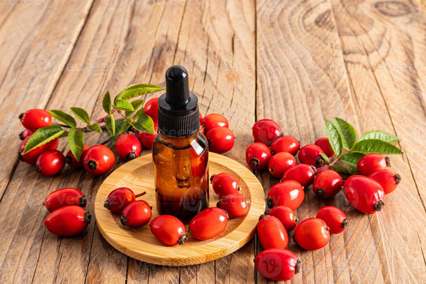 produto cosmético para cuidados com a pele facial em uma garrafa de vidro com uma pipeta em uma placa de madeira entre os frutos de rosa mosqueta madura. nutrição intensiva. foto