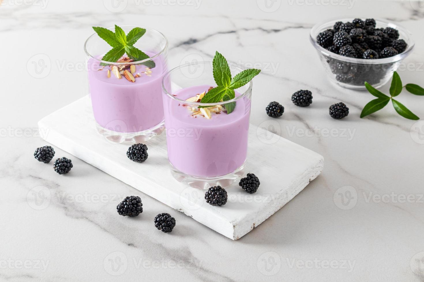 milkshake de amora ou smoothie em dois copos de vidro em uma placa de madeira branca e mesa de mármore. o conceito de alimentação saudável. foto