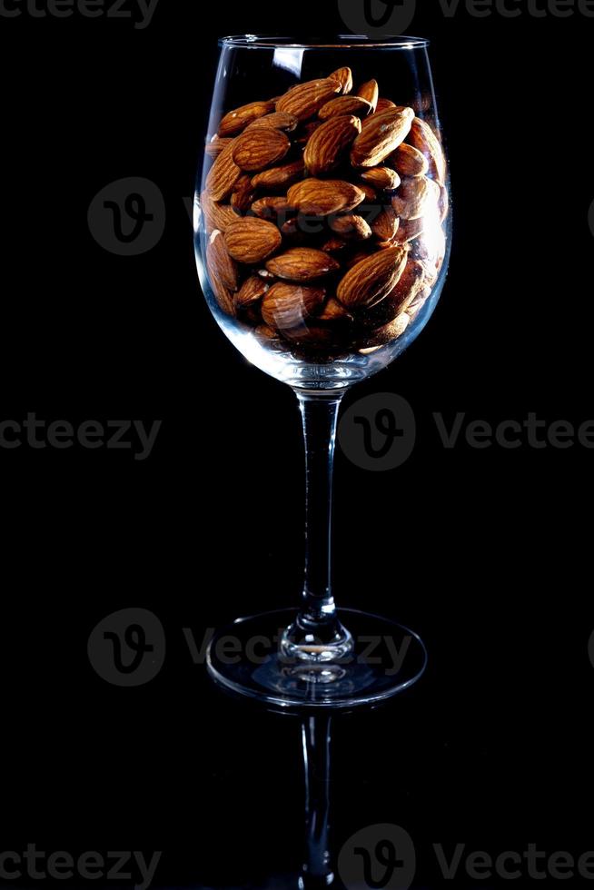 amêndoa descascada no balde de copo de vinho jar em um fundo preto isolado. linha de tigelas com amêndoas, vista frontal. foto