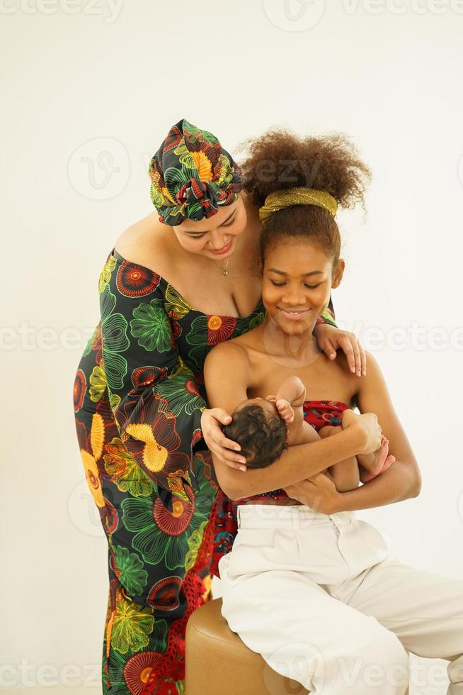 mãe e filha mais velha em vestido tradicional estilo nativo africano carregam bebê recém-nascido de um mês de idade. afro-asia de raça mista infantil feliz durma bem no abraço caloroso da maternidade. foto