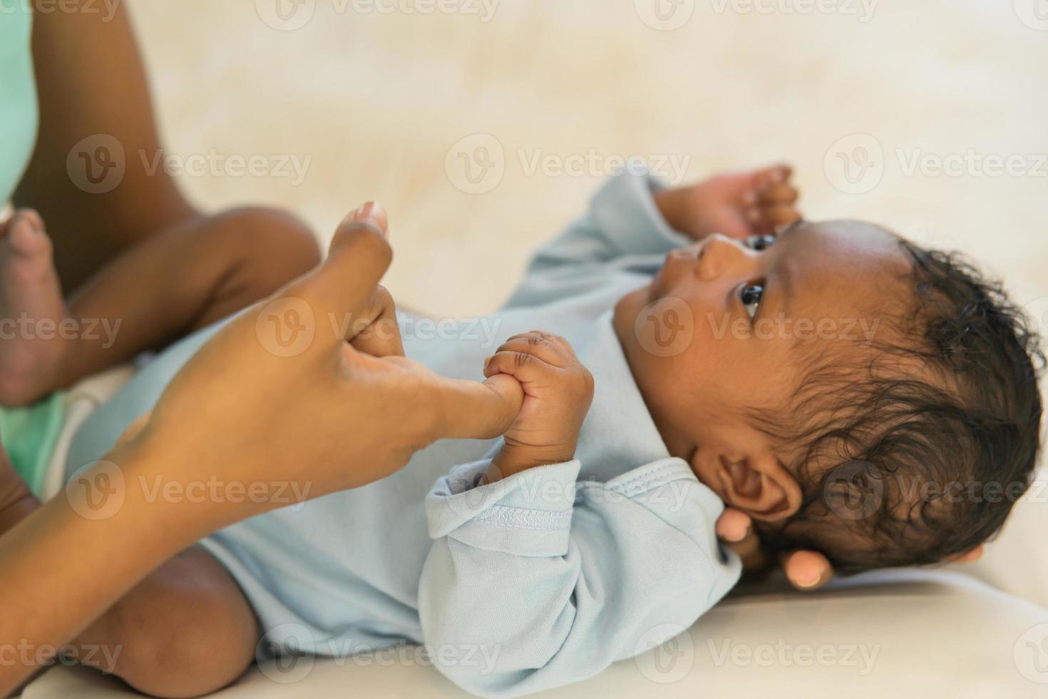 bebê recém-nascido africano de um mês segurando a mão da mãe dos dedos, sorria e olhe relaxe sem preocupações. imagem com uma profundidade de campo rasa, selecione a área de foco da mão. foto