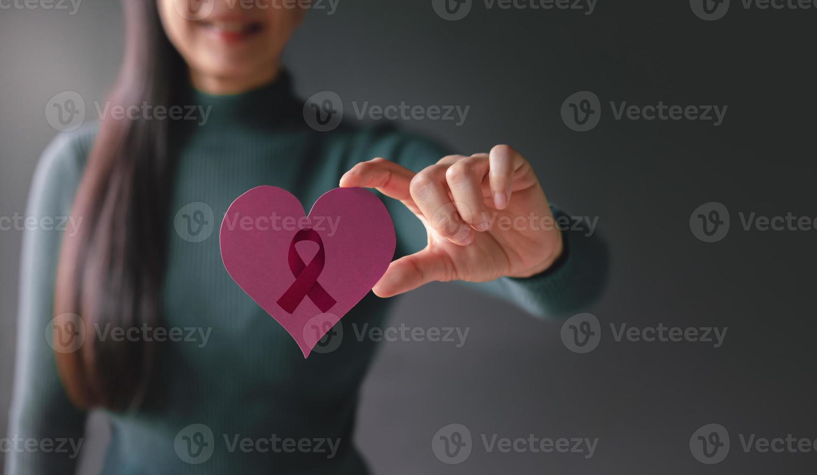 conceito de amor, saúde, câncer, doação e caridade. conscientização do câncer de mama. close-up de mulher voluntária sorridente segurando uma forma de coração com papel de sinal de fita de câncer foto