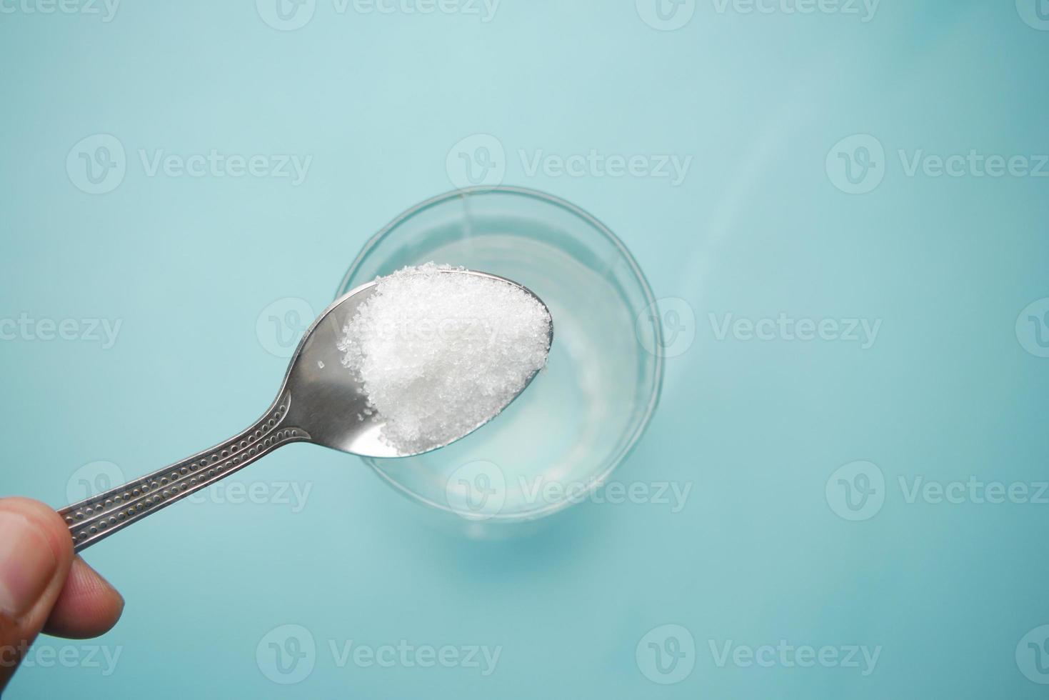 derramando açúcar branco em um copo de água na mesa foto