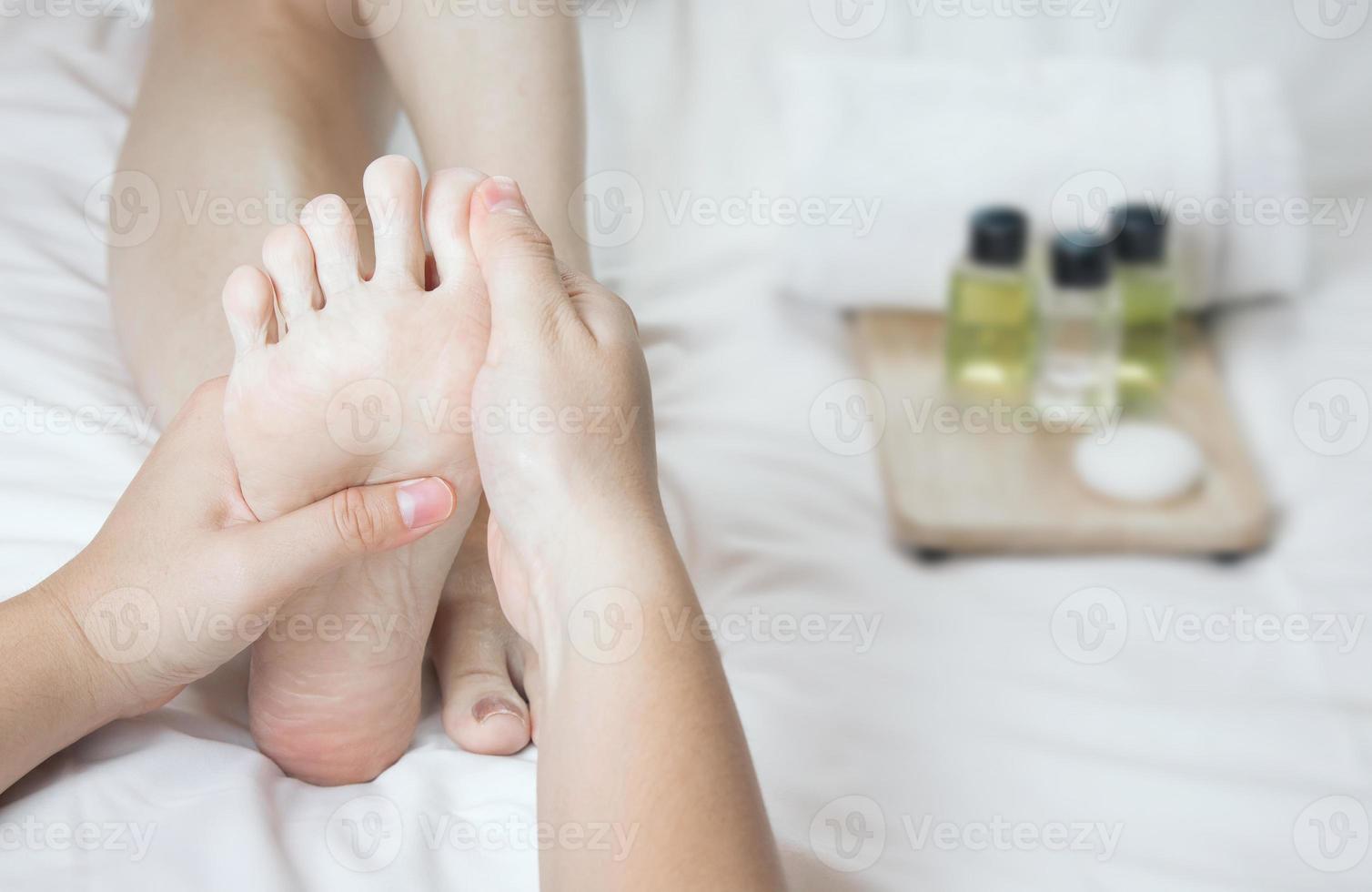 mãos de um massageador de pés profissional com óleos e produtos de saúde na cama branca. conceito de cuidados de saúde, relaxamento, tratamento de spa para os pés. ou introdução de produtos para spa de pés femininos foto