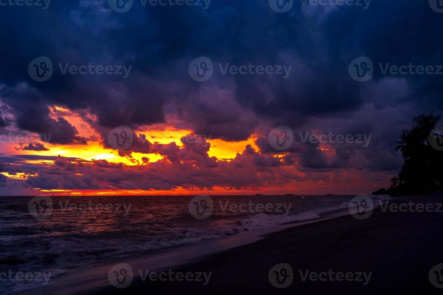 belo pôr do sol nublado na praia com palmeiras em silhueta foto