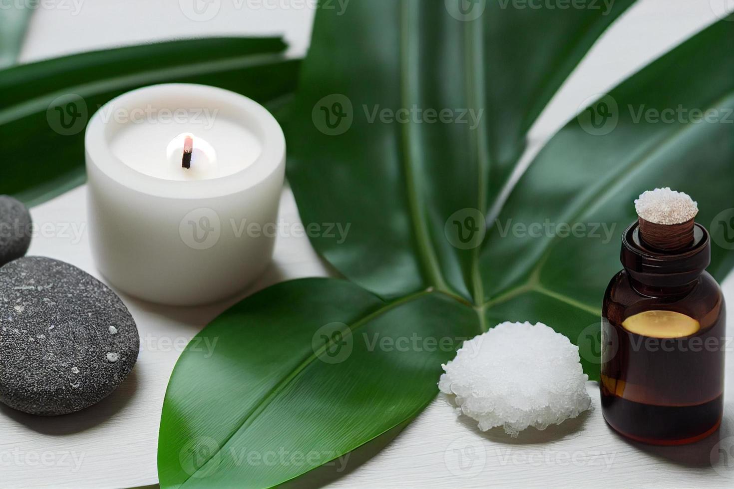 itens de tratamento de beleza para procedimentos de spa na mesa de madeira branca com planta verde. pedras de massagem, óleos essenciais e sal marinho com vela acesa. foto