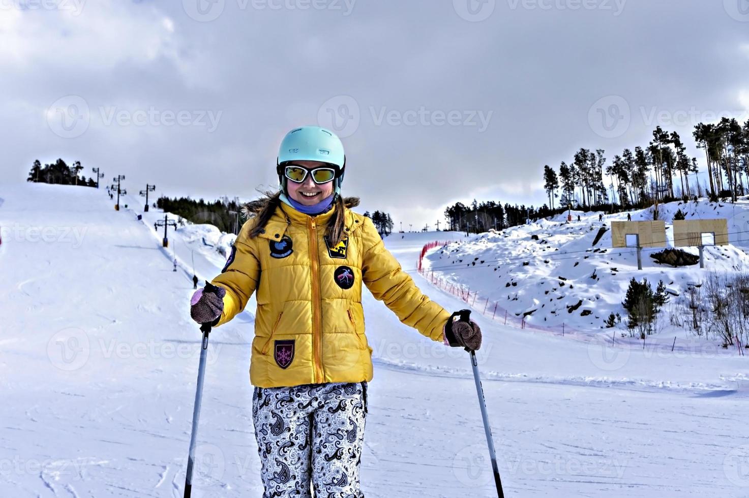 feliz sorridente jovem de jaqueta amarela e capacete de esqui esquiando em uma encosta de montanha, esportes de inverno, atividade ao ar livre de esqui alpino, estilo de vida saudável foto