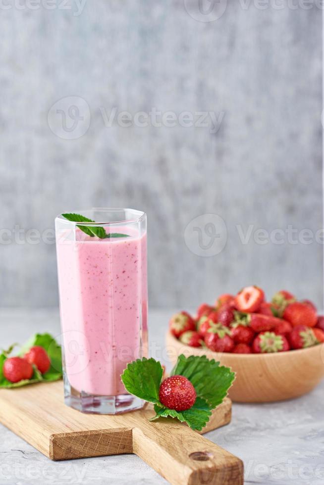 smoothie de morango em frasco de vidro e morangos frescos em tigela de madeira foto