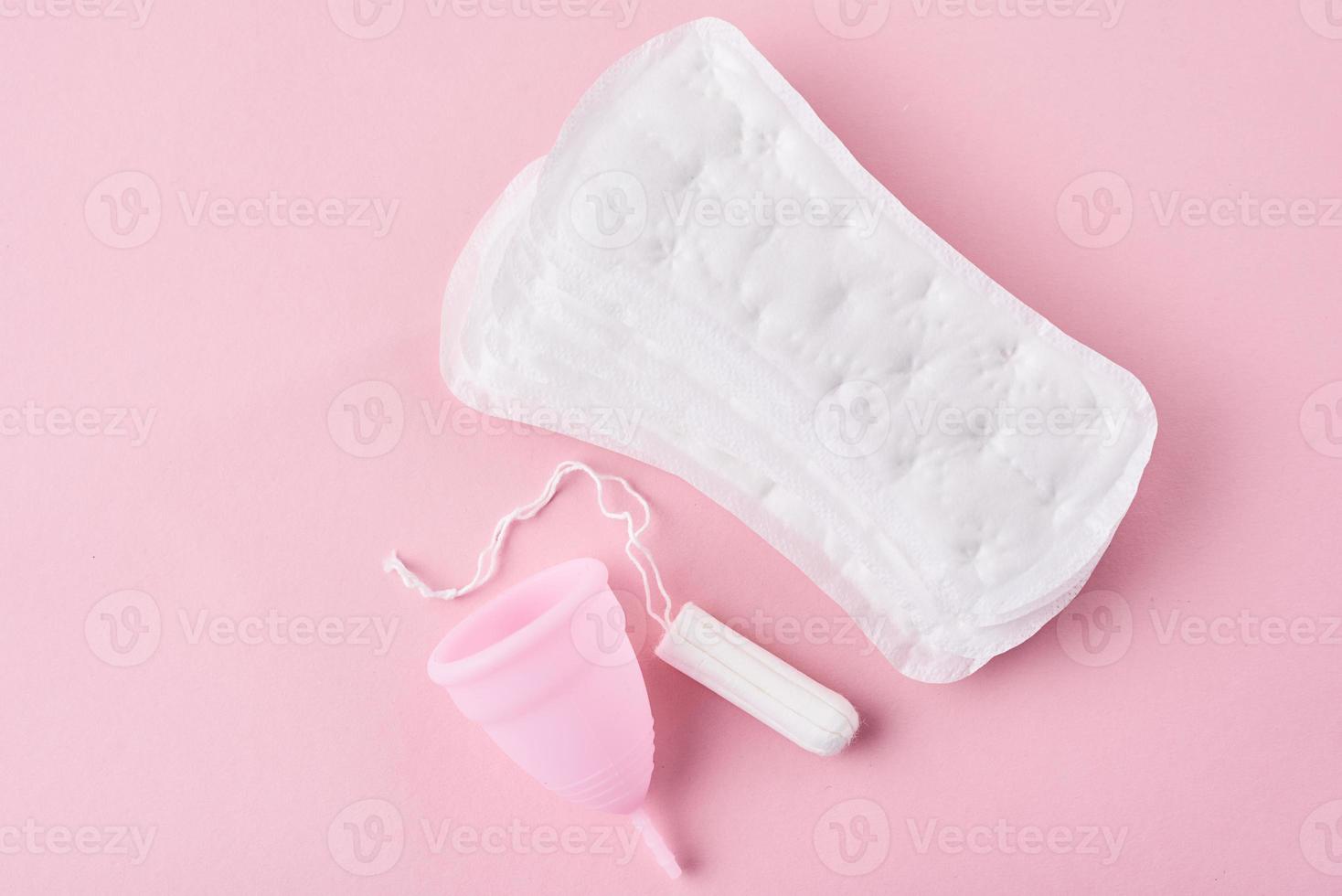 absorvente higiênico, copo menstrual e tampão em um fundo rosa foto