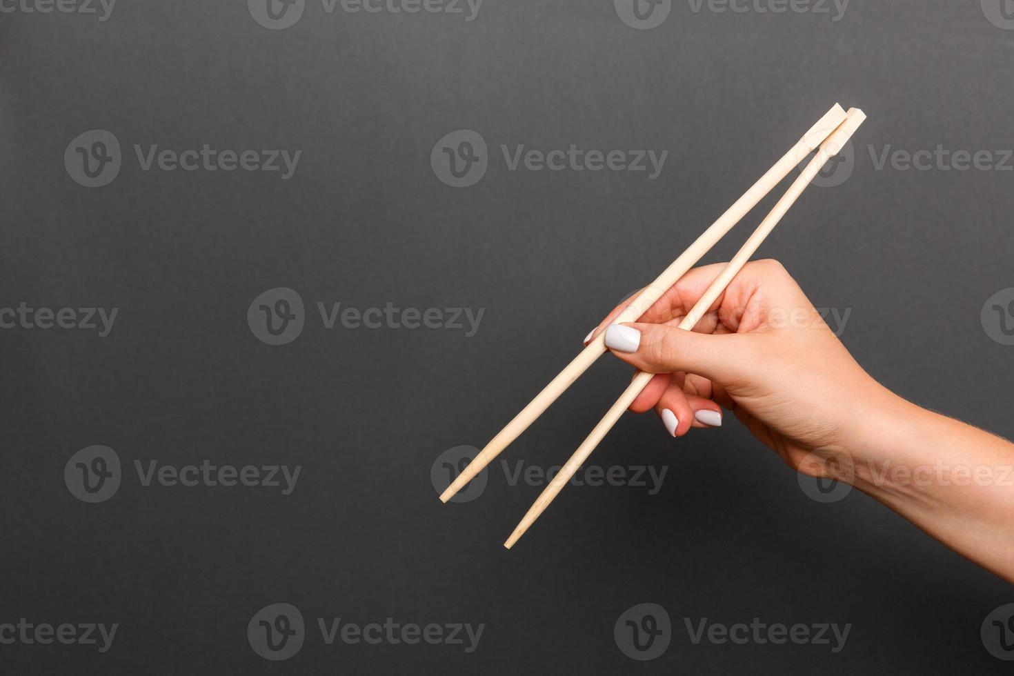 imagem criativa de pauzinhos de madeira na mão feminina em fundo preto. comida japonesa e chinesa com espaço de cópia foto