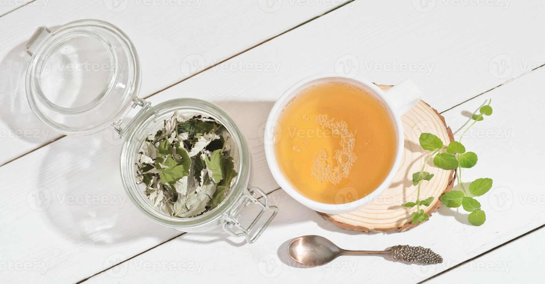 chá de ervas verde em caneca branca com folhas frescas e secas de hortelã e framboesa. chá de ervas naturais para um café da manhã saudável. vista do topo foto