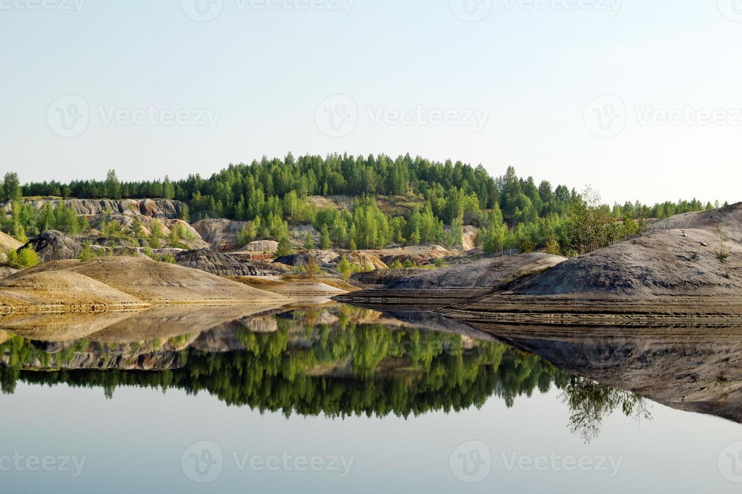 vista em uma pedreira inundada com água azul e reflexo de colinas e floresta. foto