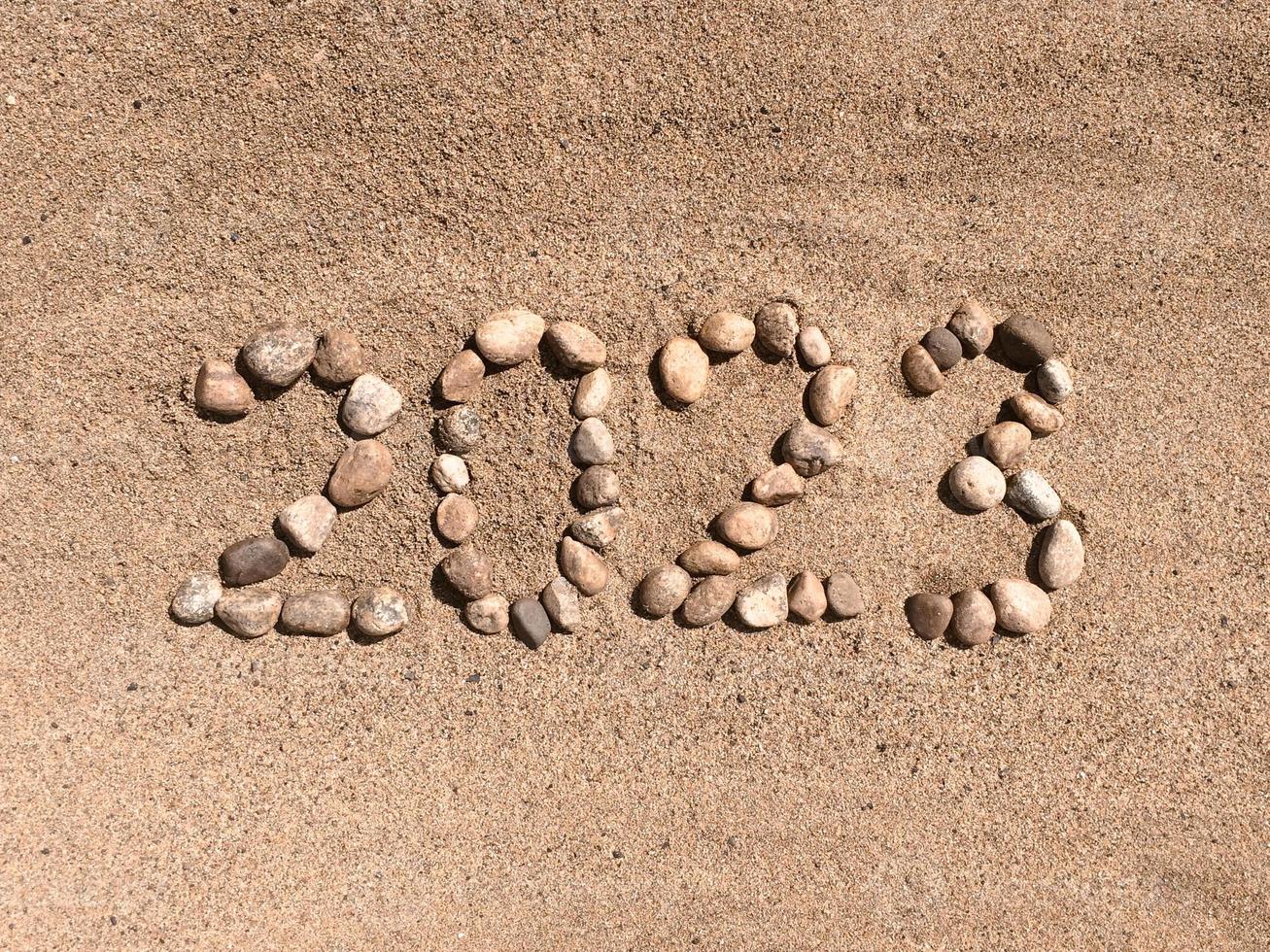 os números 2023 estão escritos e alinhados com pedras na areia. lugar para o seu texto. seu texto aqui. foto