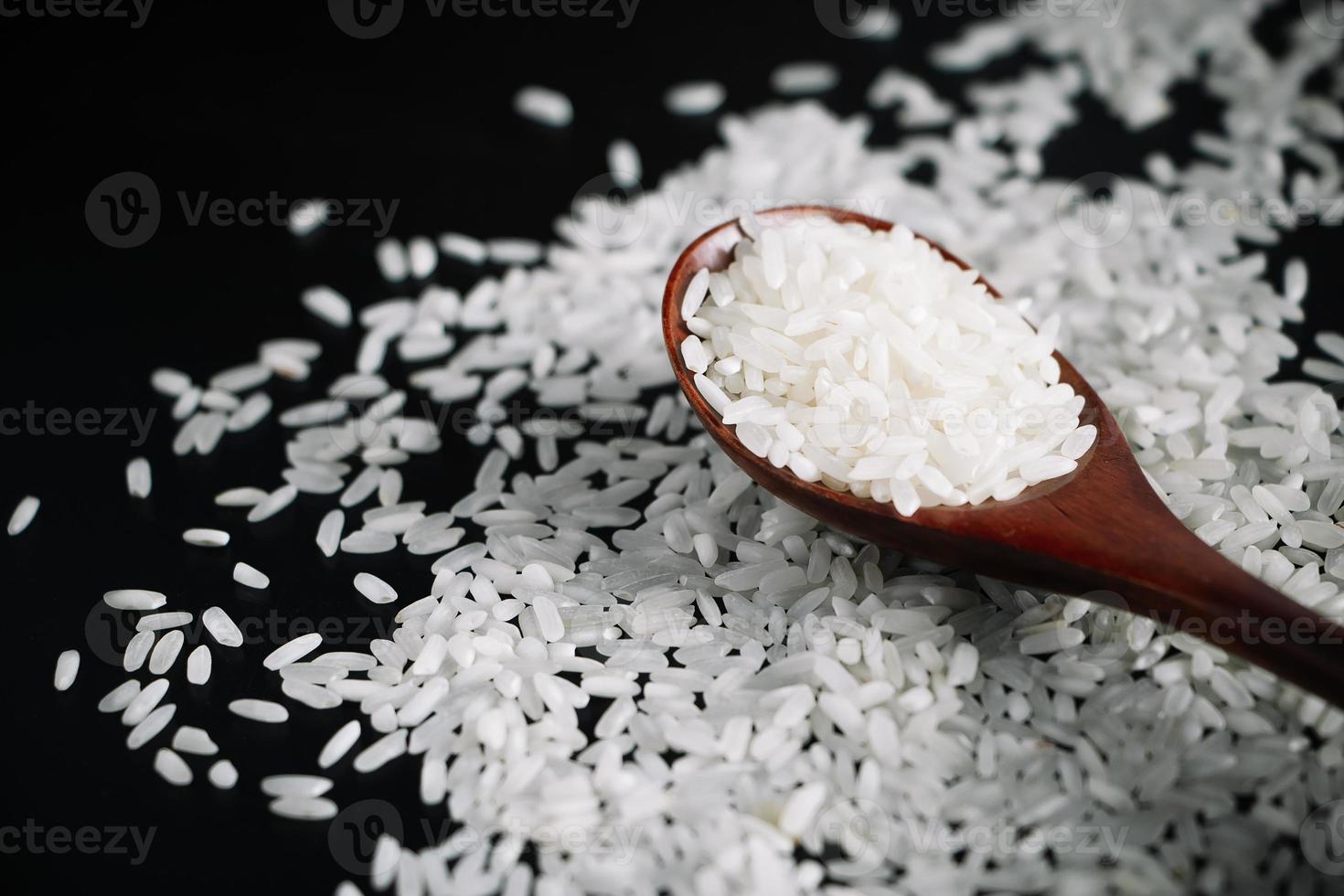 arroz branco cru na colher de pau em fundo preto. foto