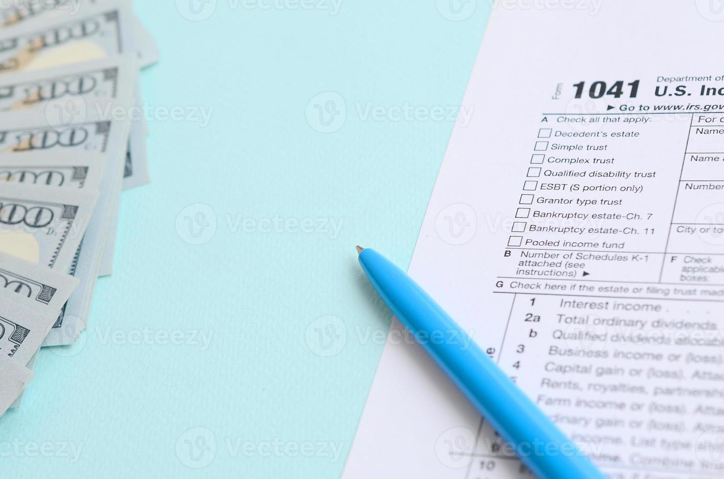 1041 formulário de imposto fica perto de notas de cem dólares e caneta azul sobre um fundo azul claro. nos retorno de imposto de renda para propriedades e fundos foto