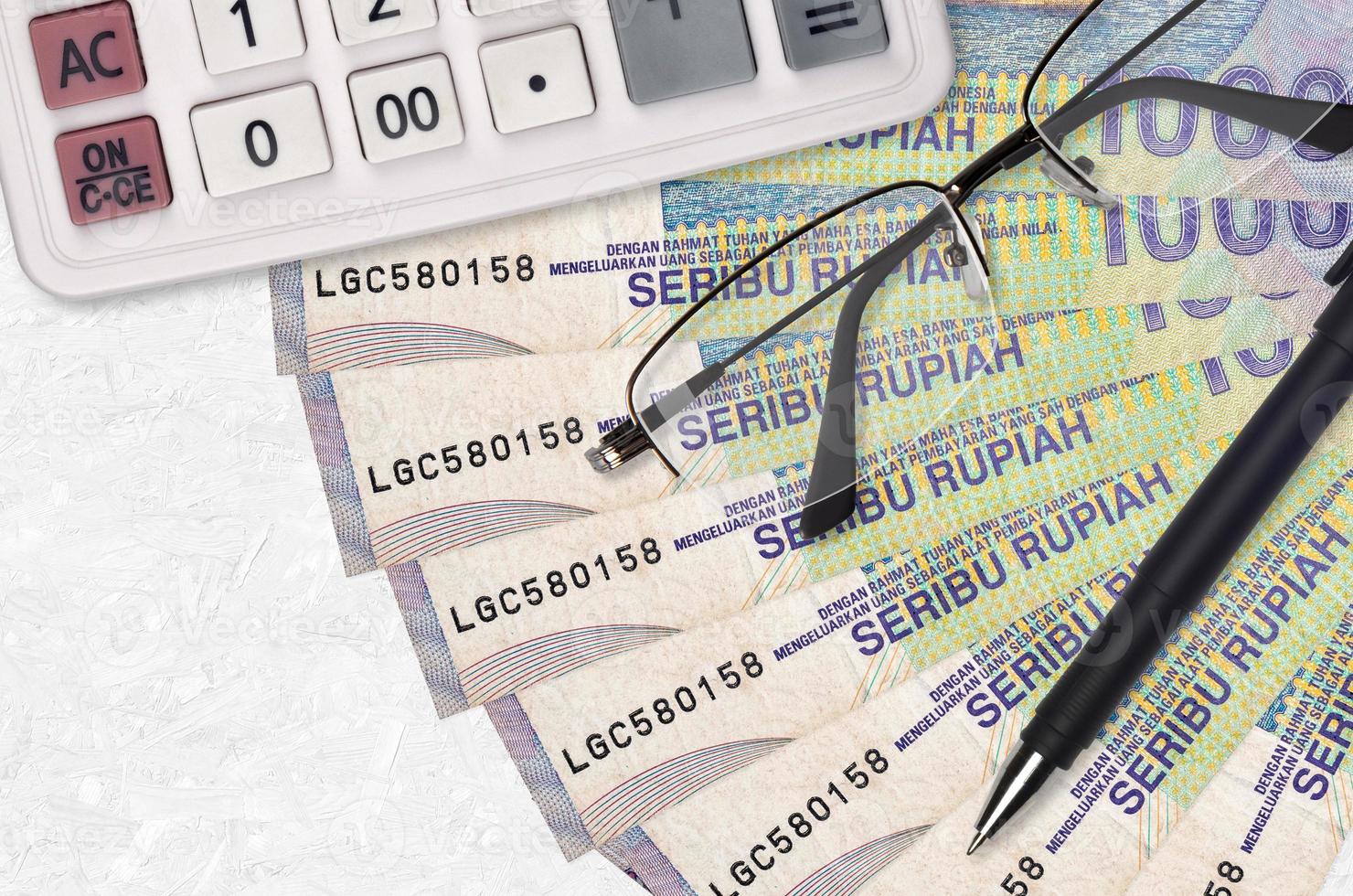 Fã de contas de 1000 rupias indonésias e calculadora com óculos e caneta. empréstimo de negócios ou conceito de temporada de pagamento de impostos foto