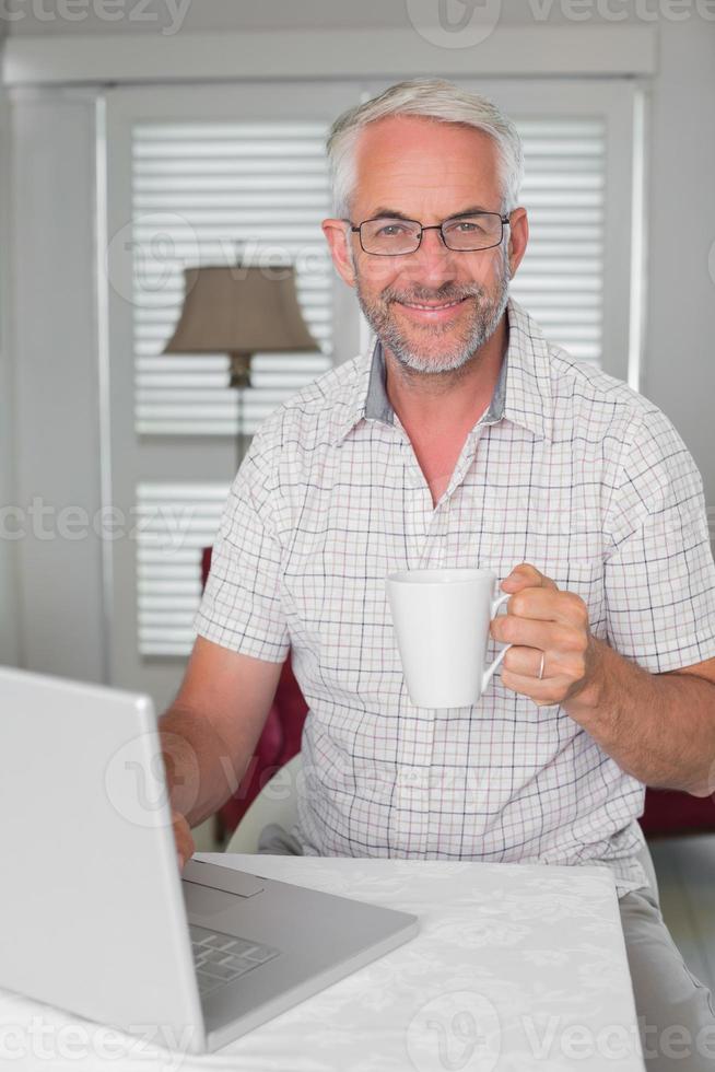 homem maduro usando laptop enquanto bebe café foto