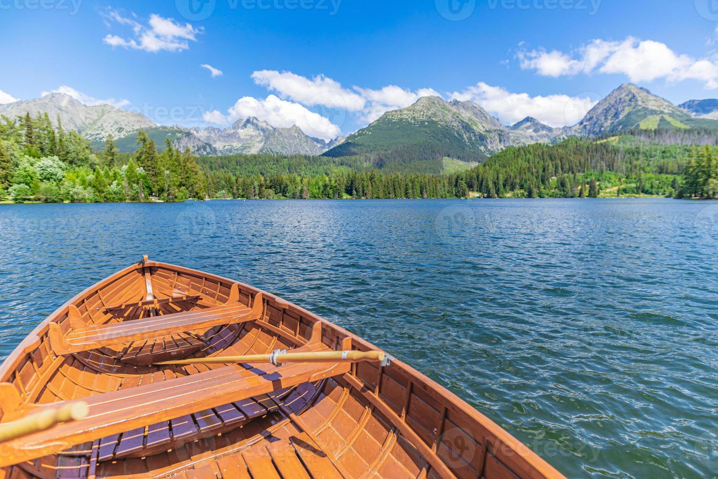 Lago de montanha com floresta de coníferas, céu azul ensolarado de barco de madeira, fundo de viagens de liberdade idílica. lugar turístico romântico. parque nacional high tatras, europa. bela paisagem natural vista idílica foto