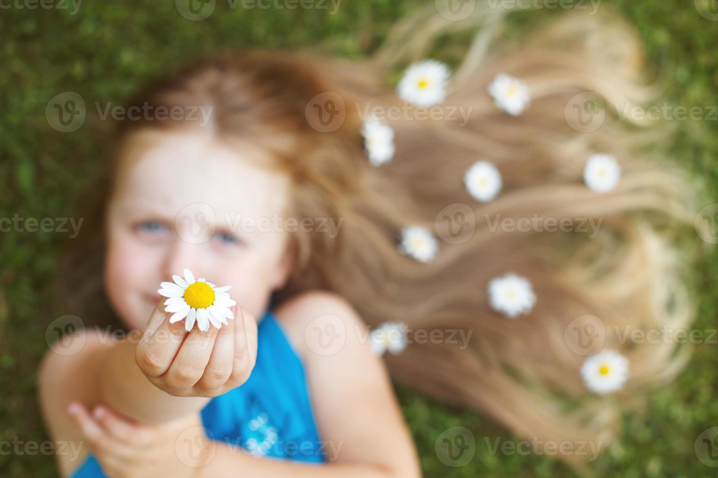 retrato de uma linda garotinha com cabelo vermelho saudável com flores de camomila deitada na grama foto