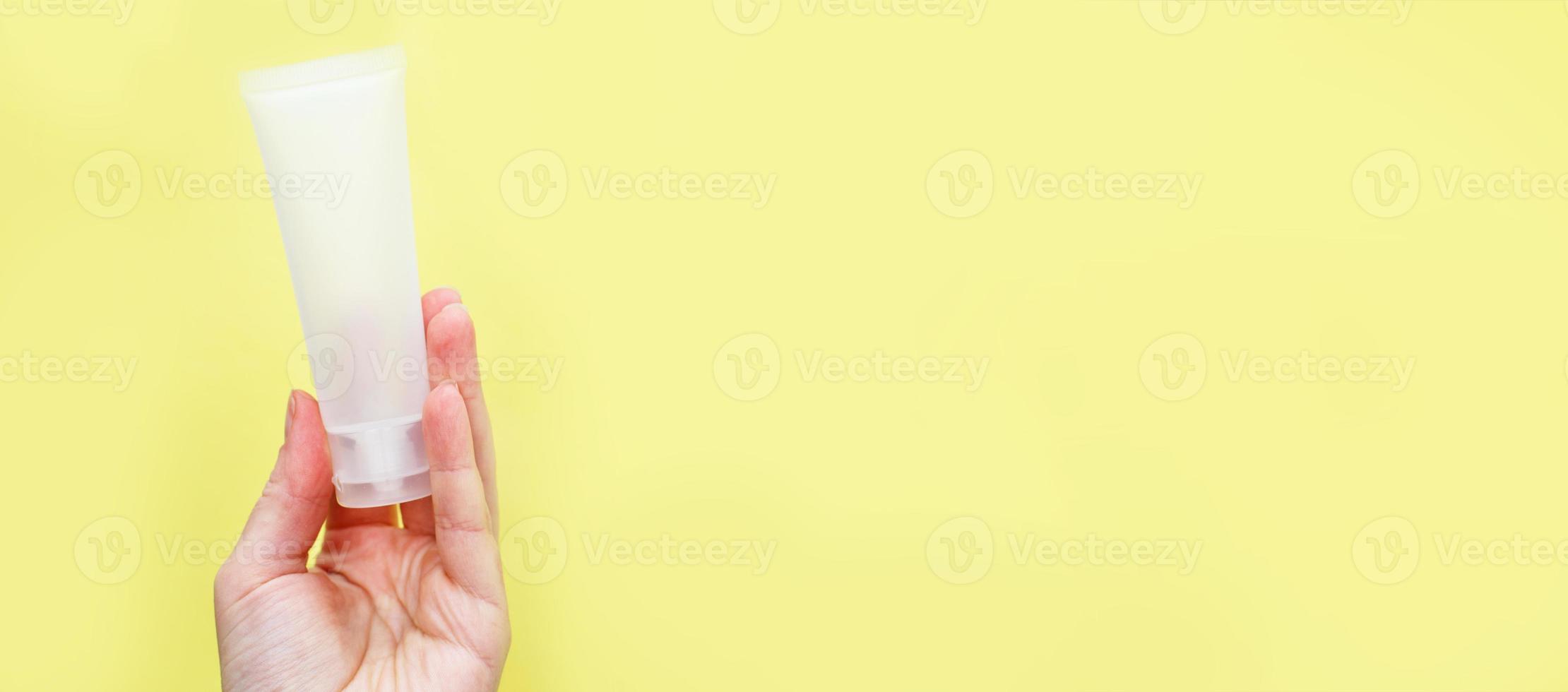 mão feminina segurando produtos cosméticos de tubo de creme em fundo amarelo. bandeira foto