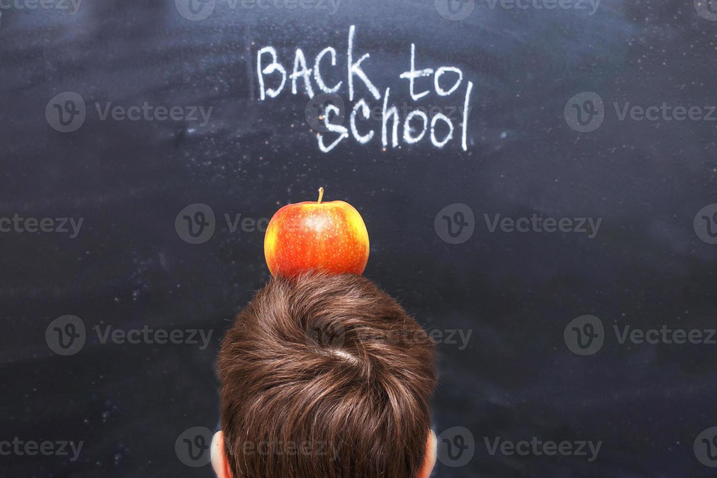 uma maçã na cabeça de uma criança perto do quadro-negro. de volta ao fundo do conceito de escola foto