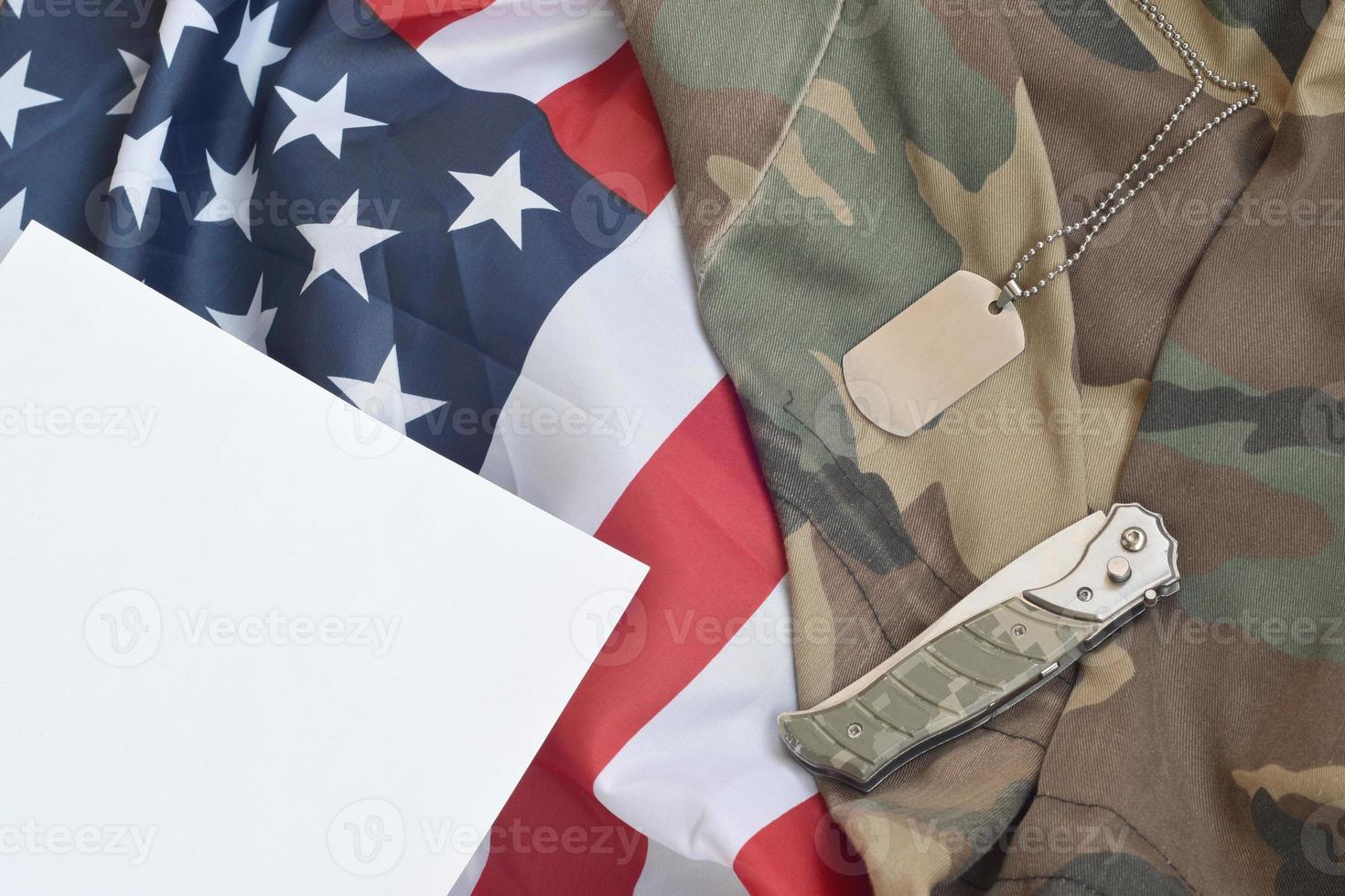 o token e a faca da etiqueta do cão do exército encontram-se no uniforme de camuflagem antigo e na bandeira dos estados unidos dobrada foto