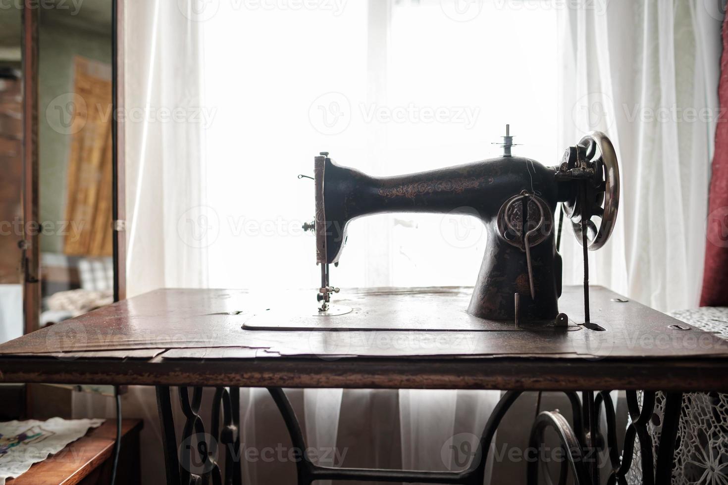 máquina de costura mecânica vintage com mesa fica perto de uma janela em uma casa rústica. foto