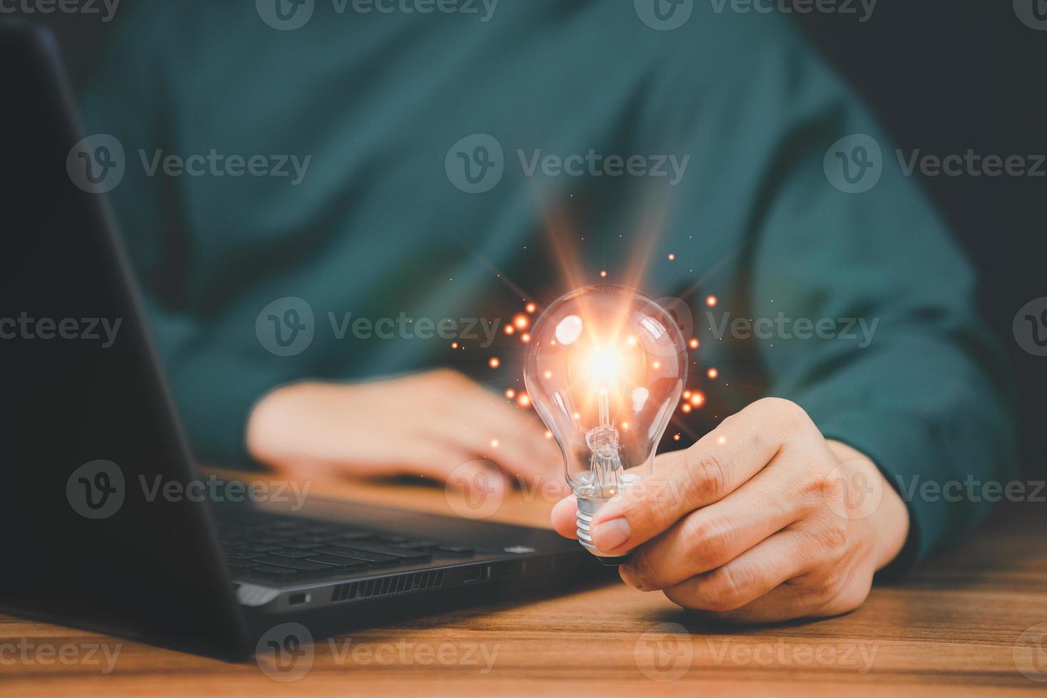 homem segurando uma lâmpada enquanto trabalha no computador para pensar e criar novas ideias com inovações tecnológicas e ideias de criatividade inspiradas em tecnologia online, inovações. foto