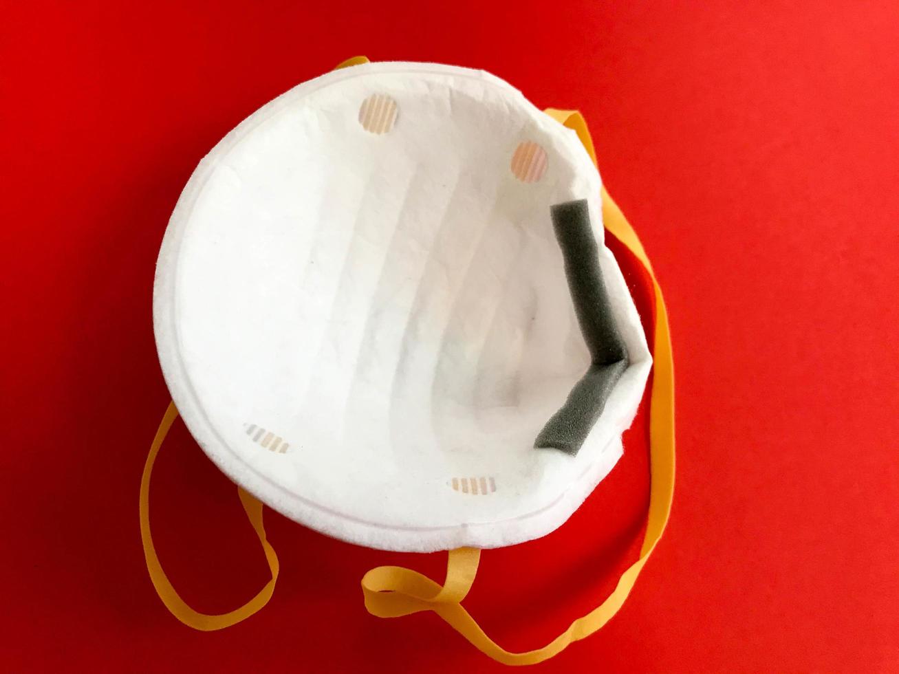 máscara médica protetora branca descartável para proteção contra doenças mortais perigosas de micróbios e vírus com coronavírus covid-19 em um fundo vermelho foto