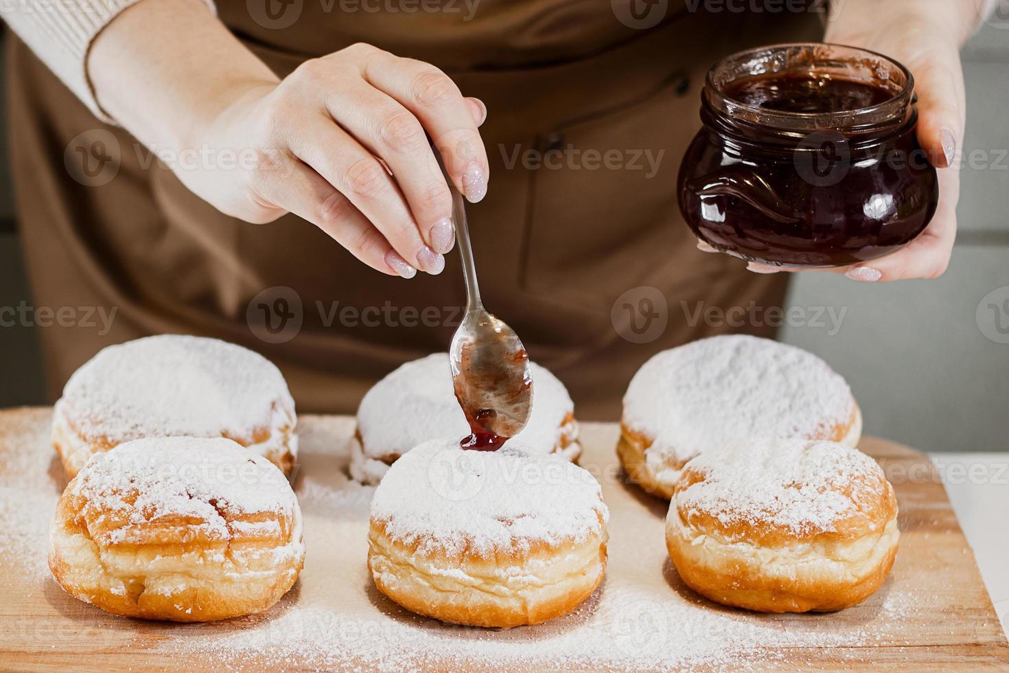 cozinhar sufganiyot de hanukkah tradicional. mulher decora rosquinhas com geléia. sobremesa judaica festiva. foto