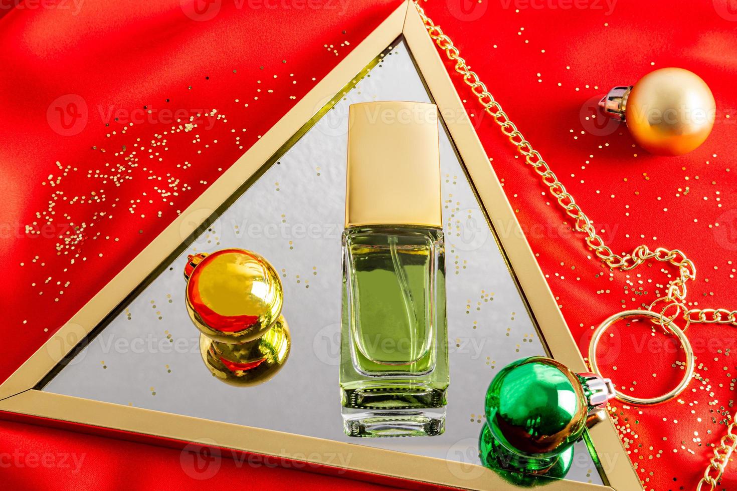 uma garrafa cosmética de água de toalete encontra-se em um espelho com bolas de vidro de natal. fundo de cetim de tecido vermelho. conceito de publicidade. foto