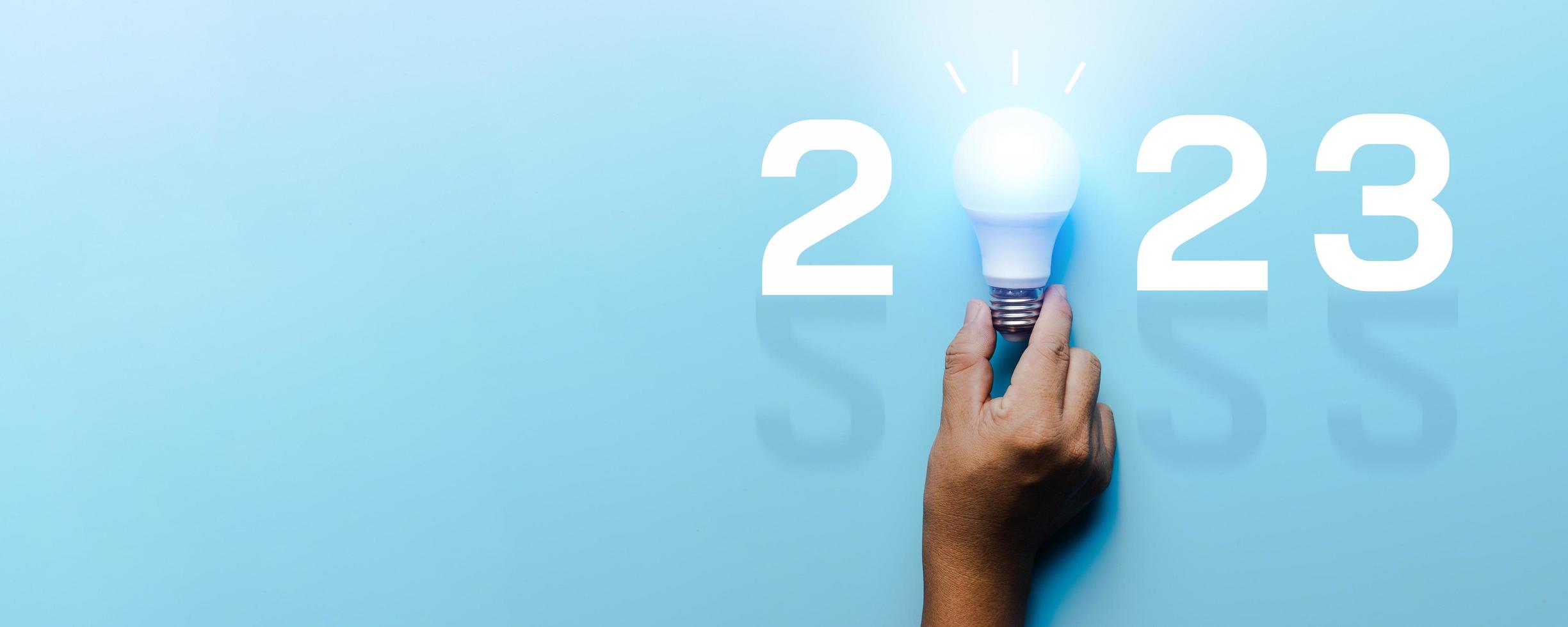 ideia e criativo em 2023, lâmpada de iluminação com número de ano novo em fundo azul foto