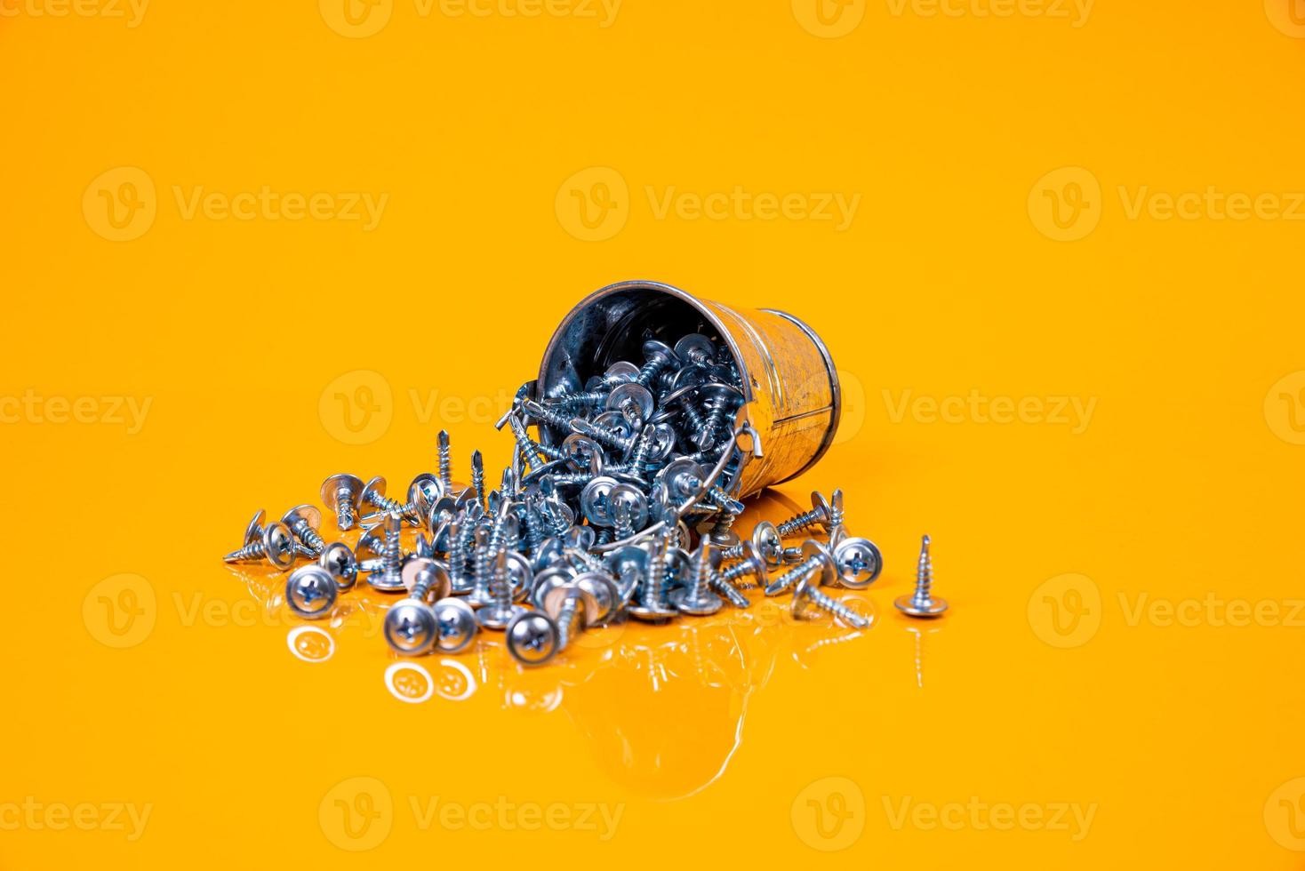 muitos parafusos auto-roscantes de metal feitos de aço em um vidro, em um balde. parafuso auto-roscante para metal, para ferro, parafuso auto-roscante cromado, sobre fundo amarelo laranja, foto