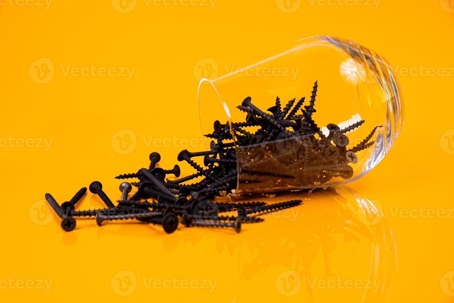 muitos parafusos auto-roscantes de metal feitos de aço em um vidro, em um balde. parafuso auto-roscante para metal, para ferro, parafuso auto-roscante cromado, sobre fundo amarelo laranja, foto