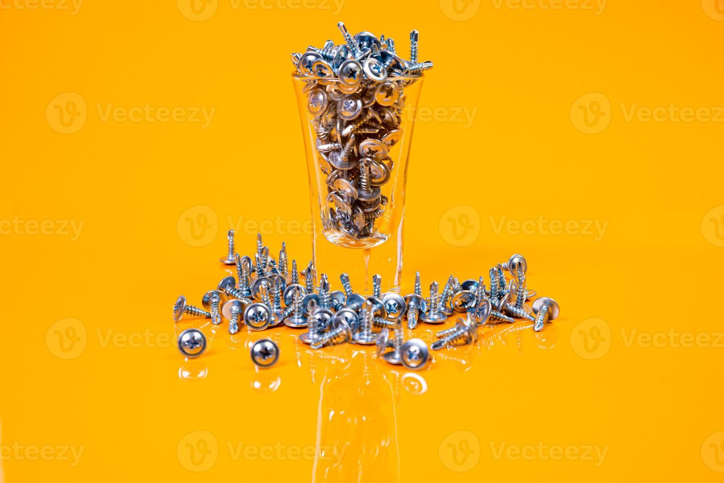 muitos parafusos auto-roscantes de metal feitos de aço em um vidro, em um balde. parafuso auto-roscante para metal, para ferro, parafuso auto-roscante cromado, sobre fundo amarelo laranja, foto