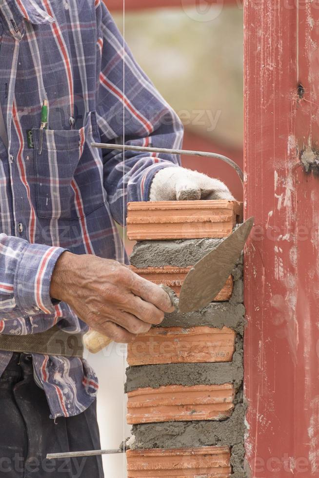 pedreiro trabalhando no canteiro de obras da parede de tijolos foto