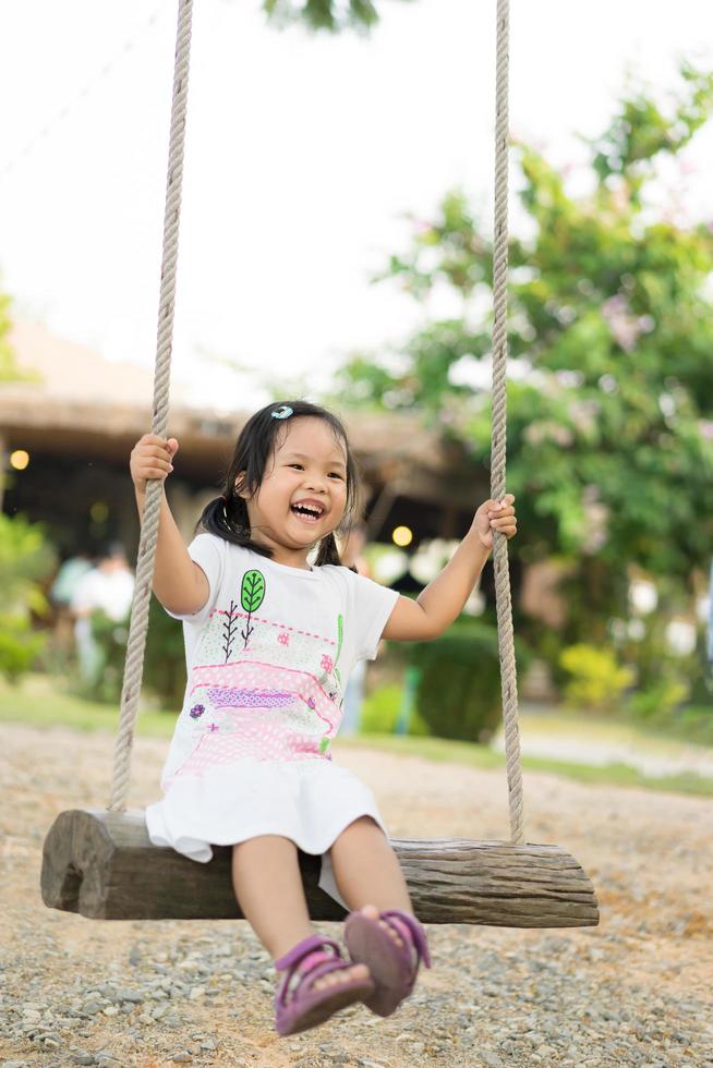 menina de vestido branco sentada em um balanço no parque foto