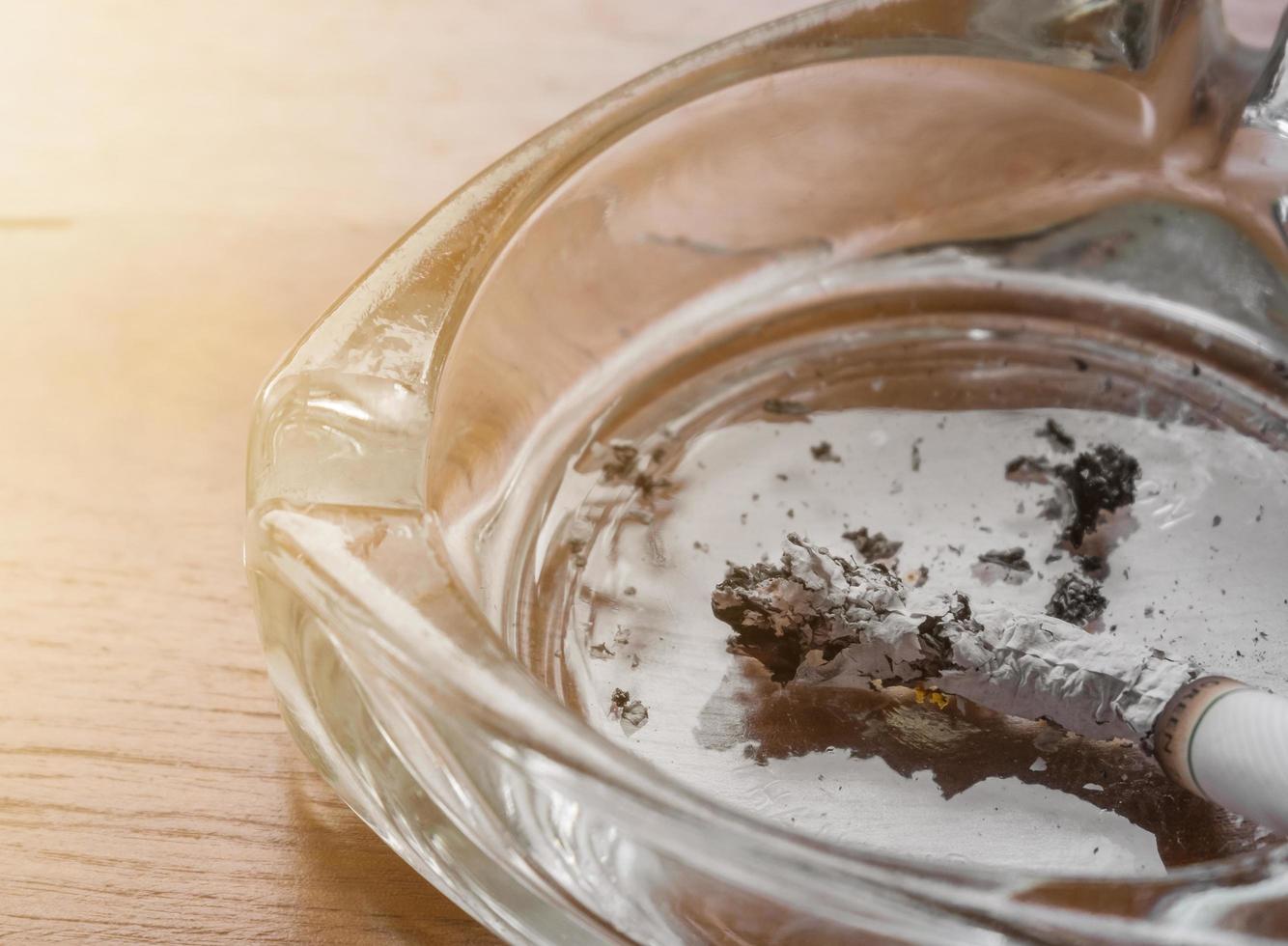 feche o cigarro colocado no cinzeiro com mesa de madeira, efeito de luz. campanha para parar de fumar conceito. foto