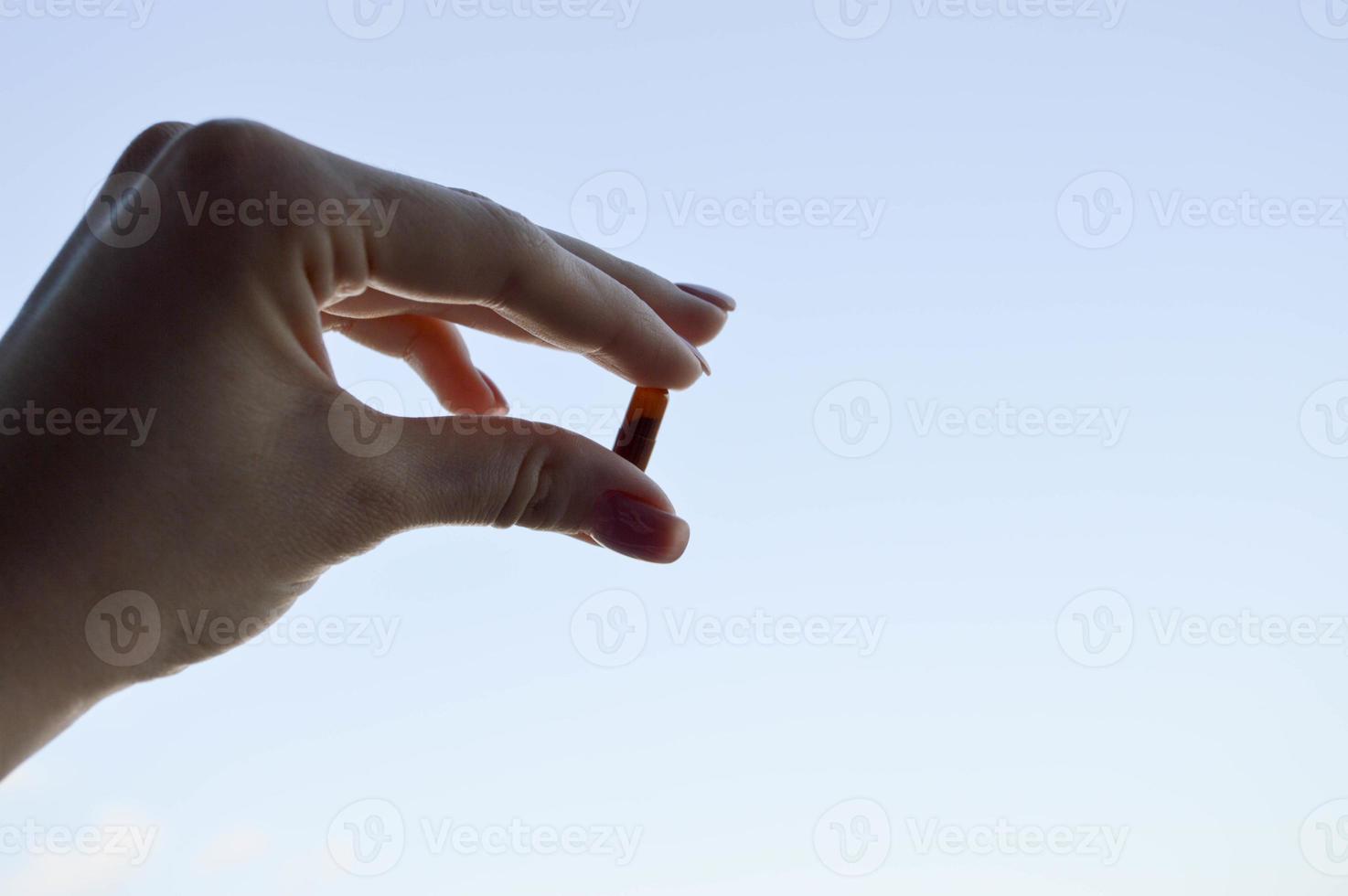 mão escurecida com um comprimido oval marrom contra o céu. medicamentos para o tratamento de doenças e patologias do corpo. curar doenças graves foto