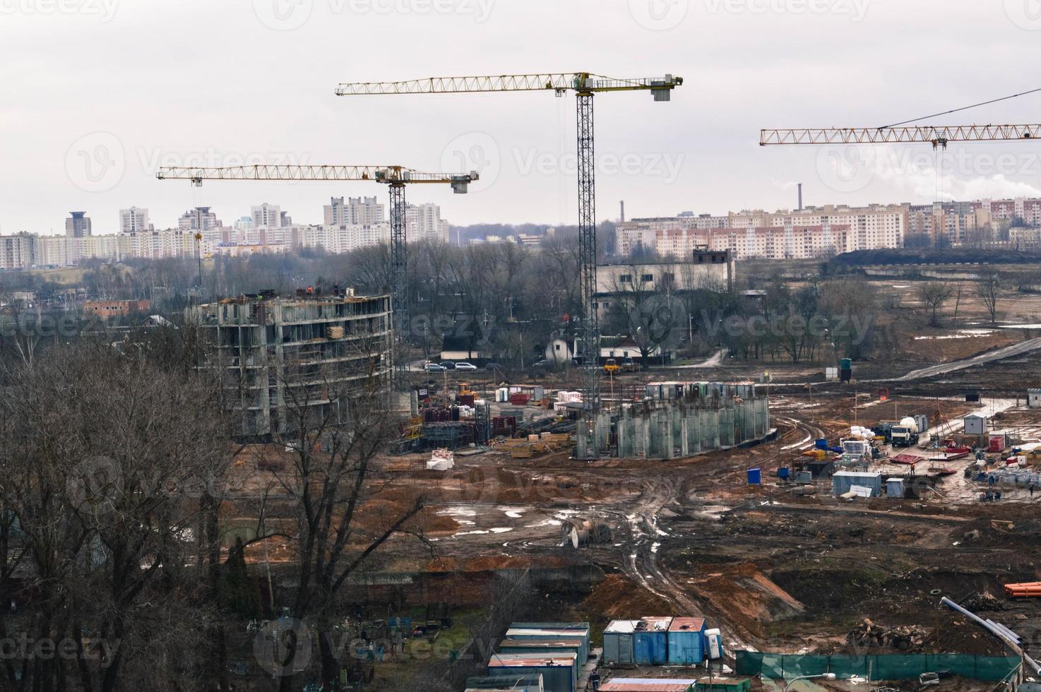 vista superior do canteiro de obras durante a construção de um novo conjunto habitacional com casas altas, novos edifícios com a ajuda de grandes guindastes industriais e equipamentos profissionais em uma cidade grande foto