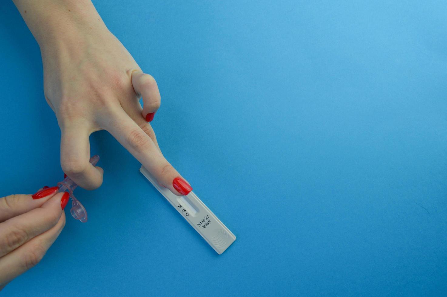 exame de sangue para o diagnóstico de coronavírus. uma garota com uma manicure vermelha brilhante aplica um dedo com uma gota de sangue após uma punção para um teste expresso. tira sensível para detectar coronavírus foto