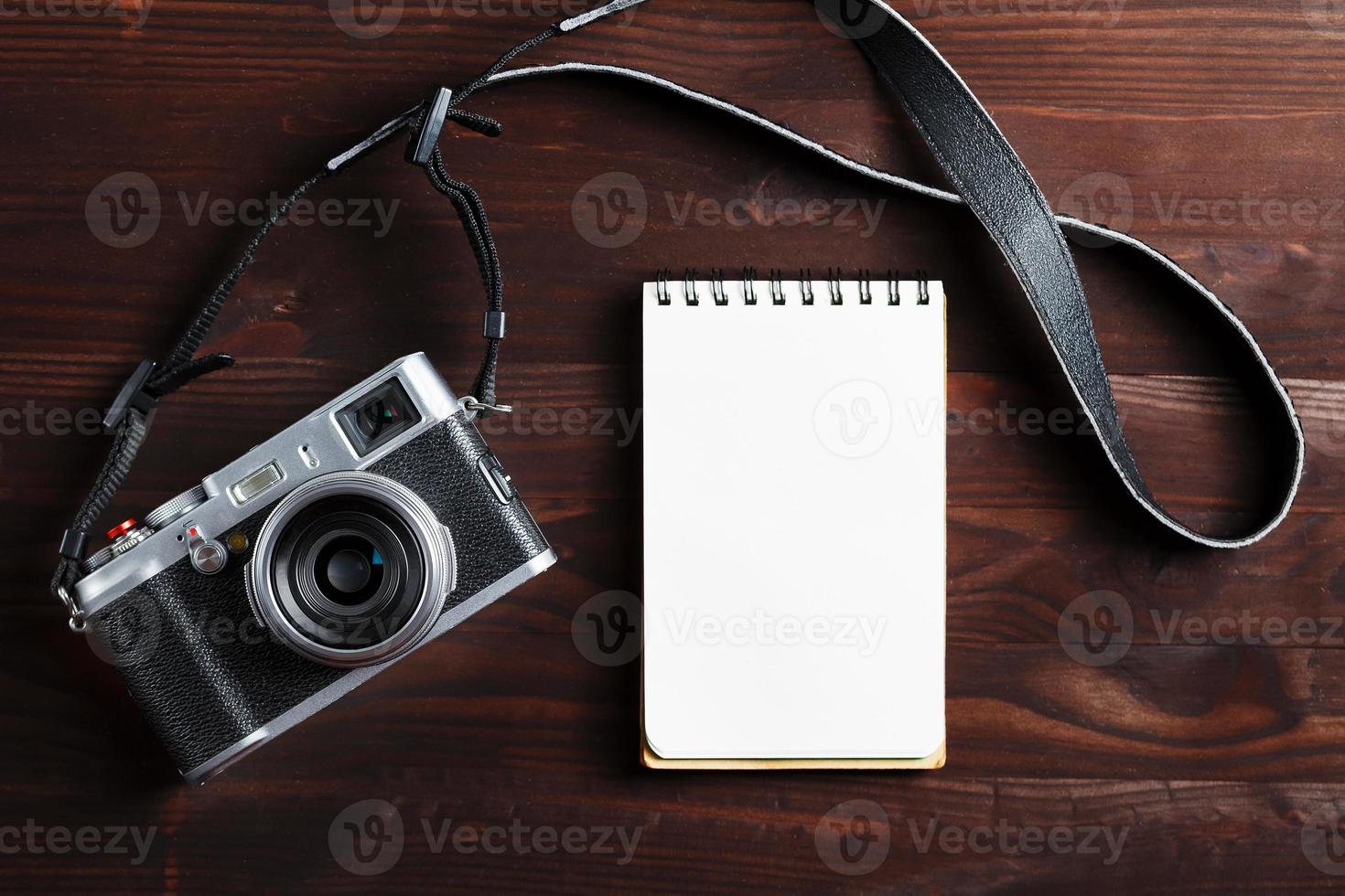página de bloco de notas em branco e câmera moderna em estilo clássico na mesa de madeira marrom escura foto