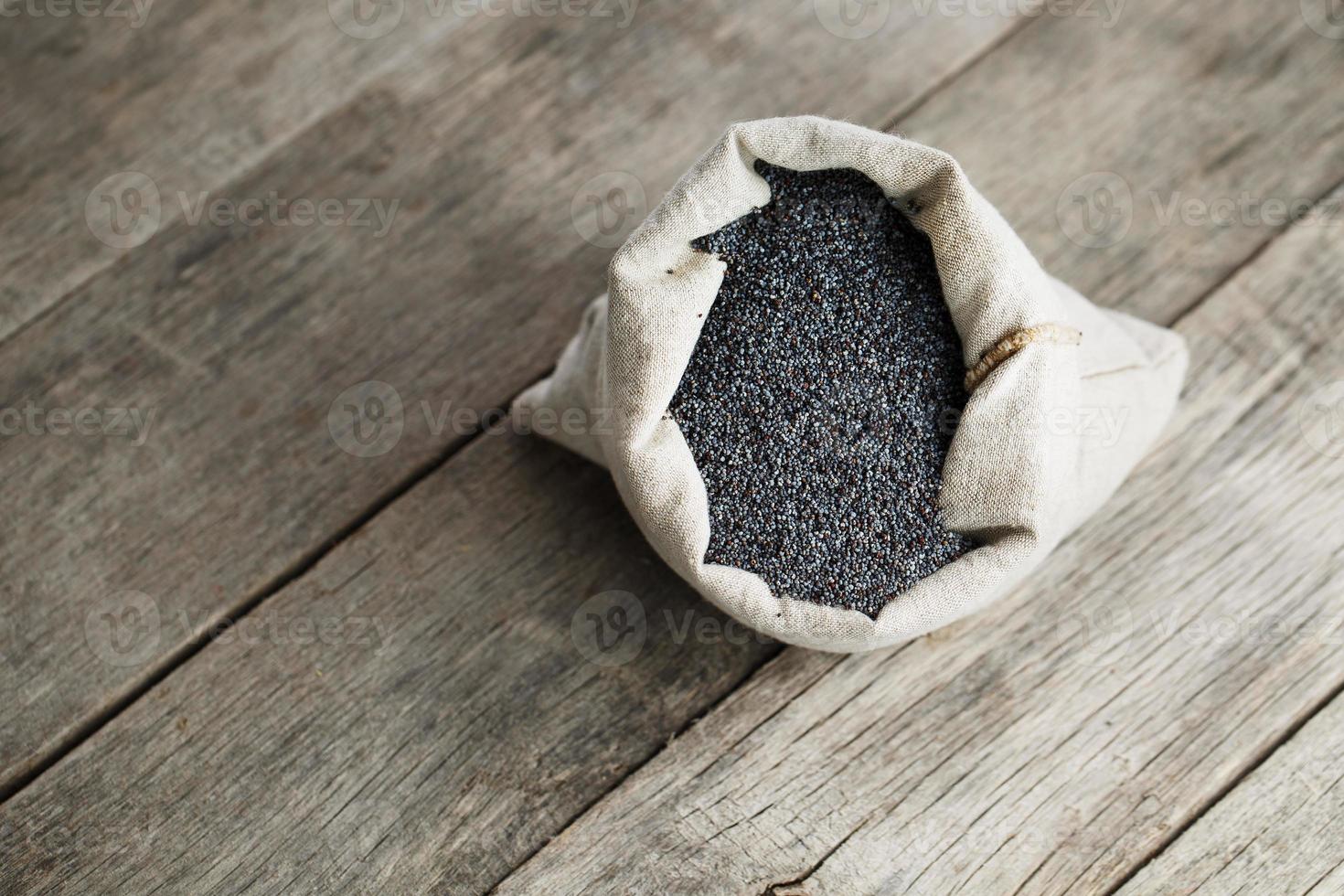 sementes de papoula em um saco de serapilheira em um fundo cinza de madeira vintage. as sementes saborosas e úteis ricas em proteínas e óleos. foto
